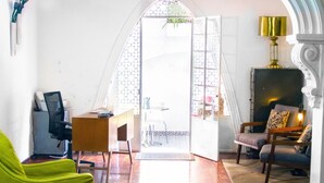 Een kamer met een houten vloer, een bureau met stoel, een groene fauteuil, een bank en een lamp.
