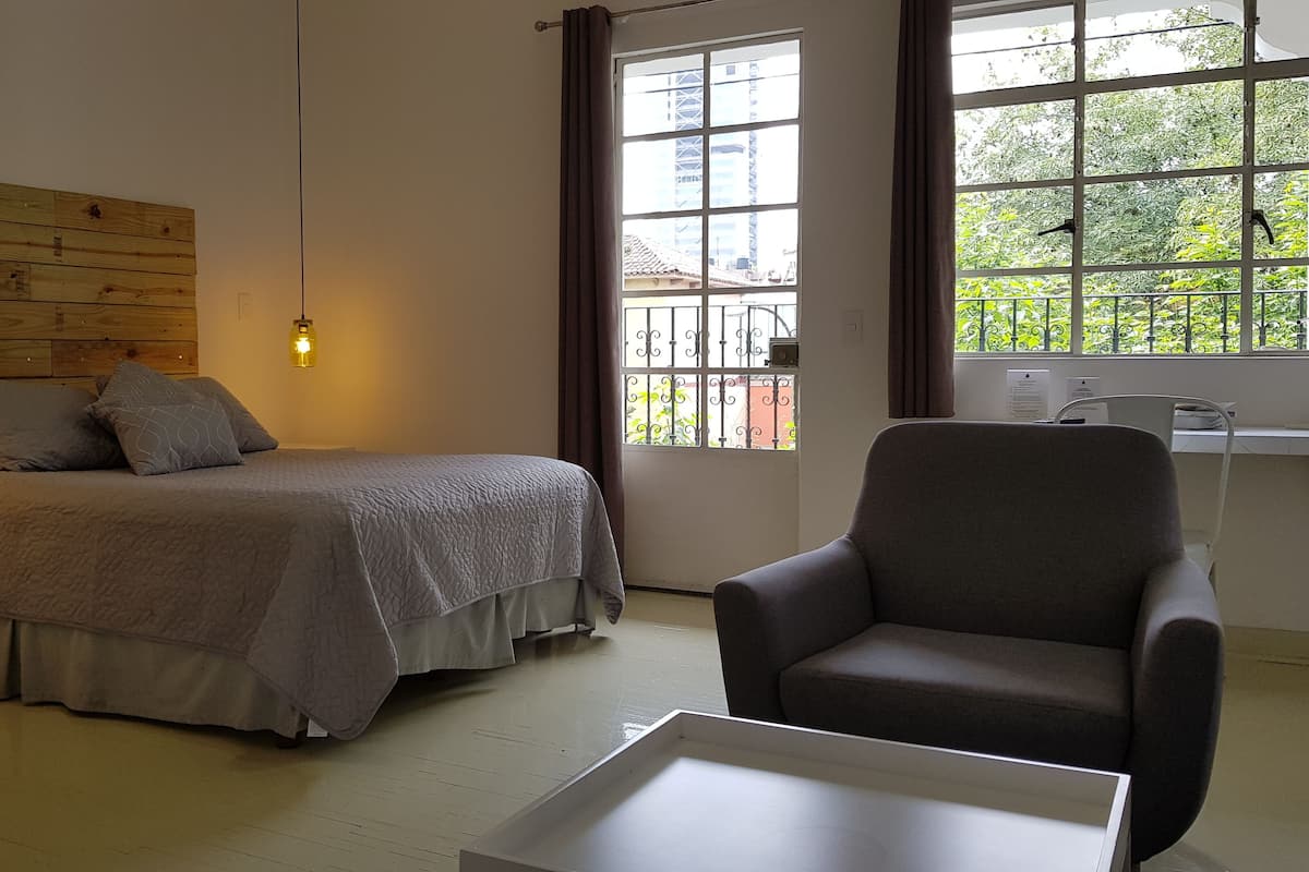 A bedroom with a bed, bedside tables, a chair, and a window with a view of greenery.