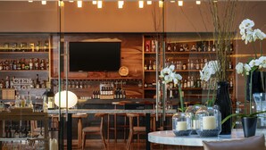 A modern bar area with a wooden bar counter, seating, and a large TV screen. - Hyatt Centric Campestre Leon (León)