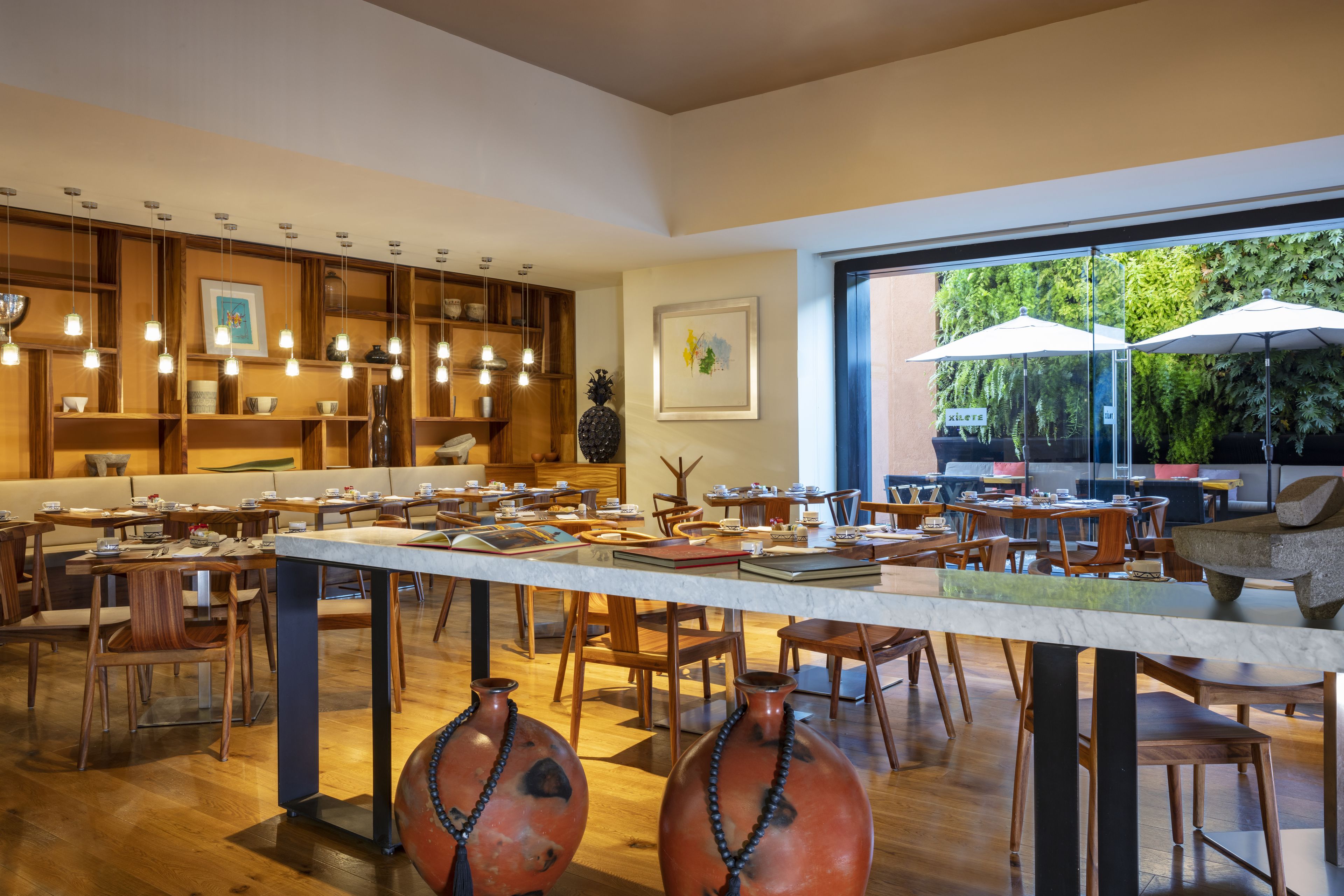 Un vaste espace dédié à la salle à manger, avec des meubles en bois, des luminaires suspendus et de grandes fenêtres offrant une vue sur l’extérieur.