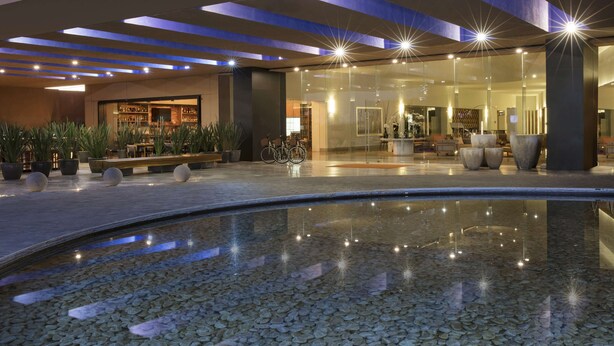 A modern hotel lobby with a central pool, seating areas, and a bar. - Hyatt Centric Campestre Leon (León)