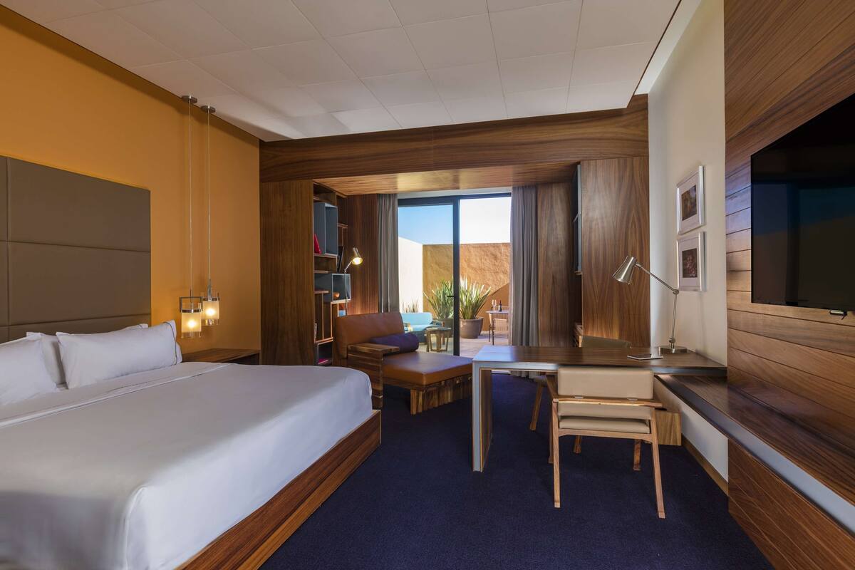 Habitación de hotel con una cama grande, un escritorio, una silla, un sofá y un televisor.
