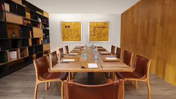 Ein Konferenzraum mit einem langen Holztisch, Ledersesseln und einem Bücherregal mit Büchern und Dekorationselementen.