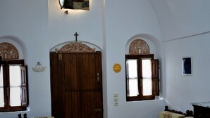 Una habitación con puerta de madera, dos ventanas con cortinas, una araña y muebles con diseños.