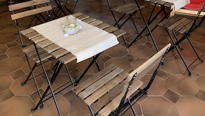 Zona de dinar amb paviment de rajoles hexagonals, taules i cadires de fusta, columna de maó i un mostrador de buffet amb diversos plats.