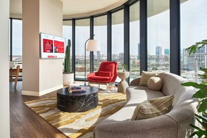 A modern living room with a curved ceiling, a red chair, a beige sofa, and a large window offering a city view.