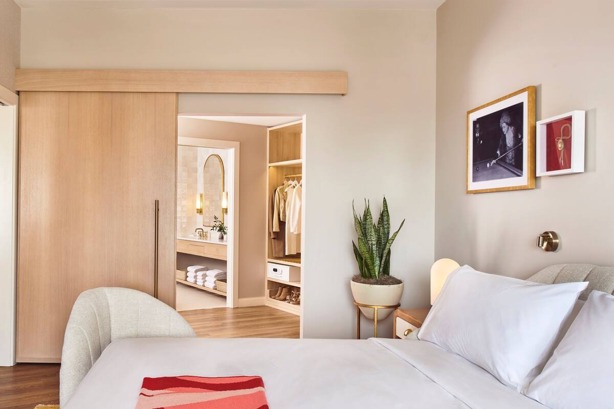 Een hotelkamer met een bed, nachtkastje, potplant, kledingkast en spiegel.