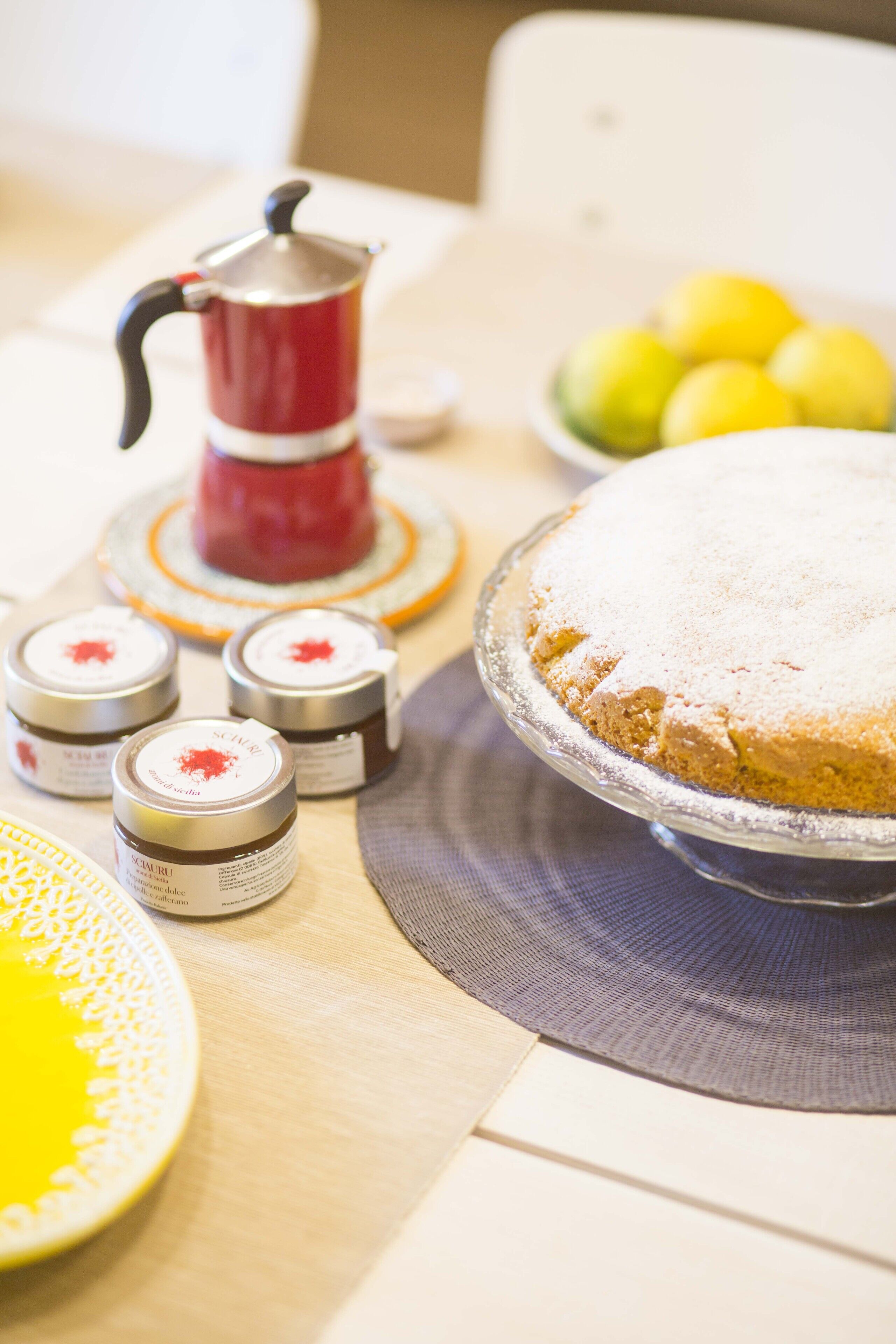 Ein Tisch mit einem runden Kuchen auf einem Präsentierteller, einem roten Teekännchen und mehreren kleinen Gläsern mit Etiketten.