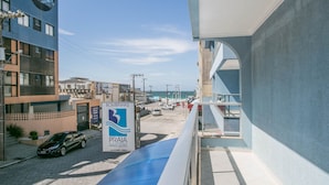 Un edificio moderno con decorazioni blu e bianche, un cartello con su scritto "BOMBINHAS PRAIA APART HOTEL" e vista sulla strada e sull'oceano.