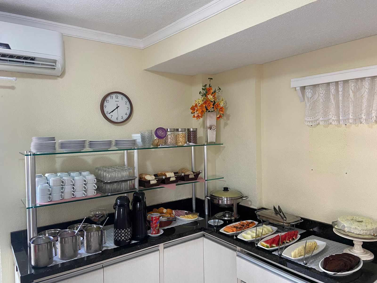 A breakfast buffet with various food items, a clock, and a vase of flowers.