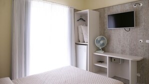 Una camera d'albergo con un letto, un armadio, una TV e un ventilatore.