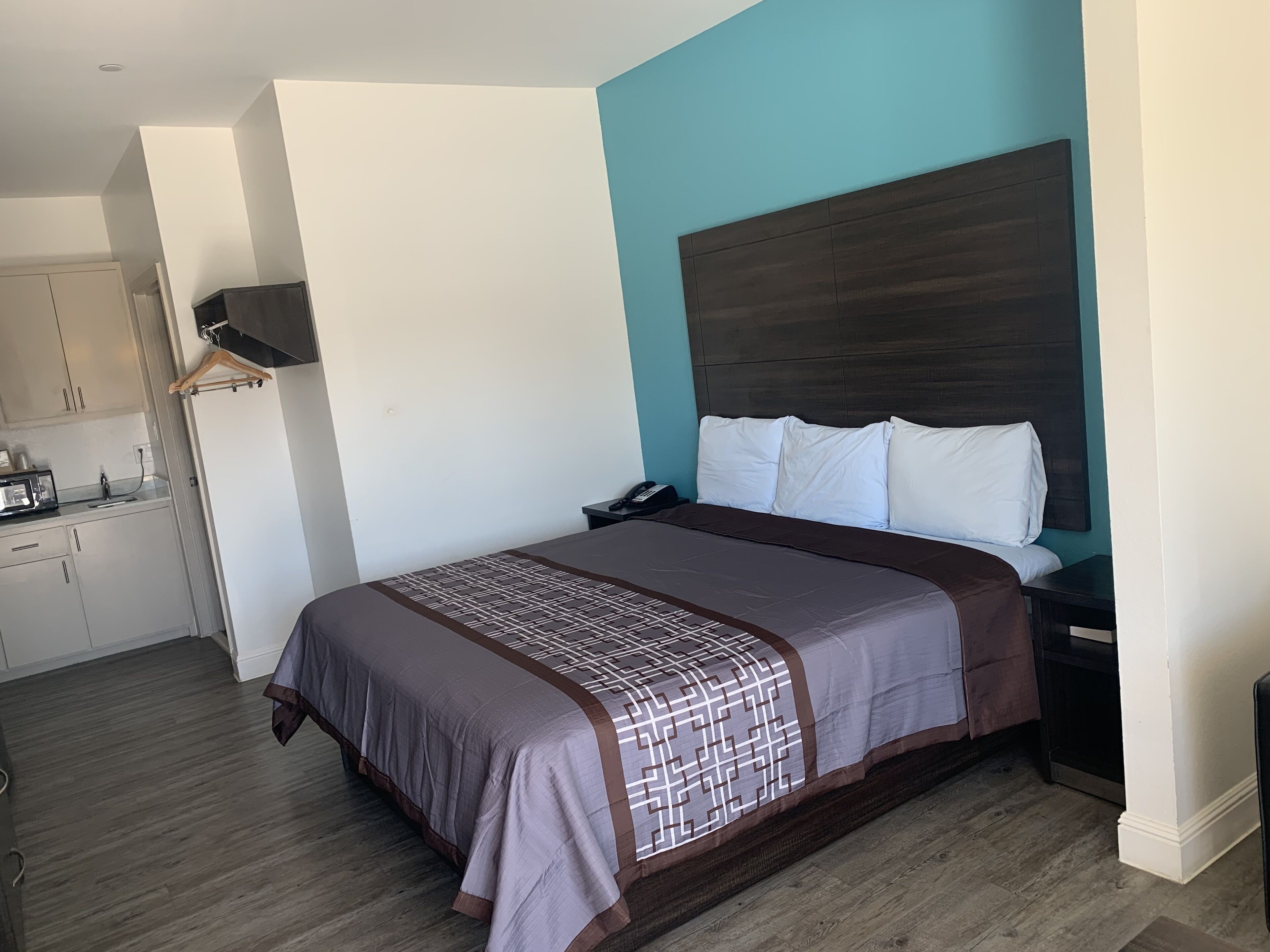 A hotel room with a bed, a bedside table, a telephone, and a small kitchenette area.