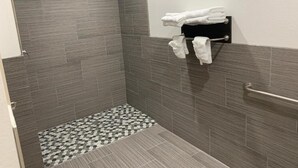 A shower with grey tiles, a towel rack with folded towels, and a patterned floor. - Lotus inn (Houston)