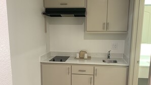 A compact kitchen with a sink, countertop, and cabinets. - Lotus inn (Houston)
