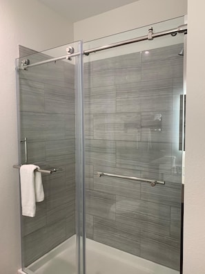 A modern shower enclosure with a glass door, a towel rack, and a showerhead. - Lotus inn (Houston)