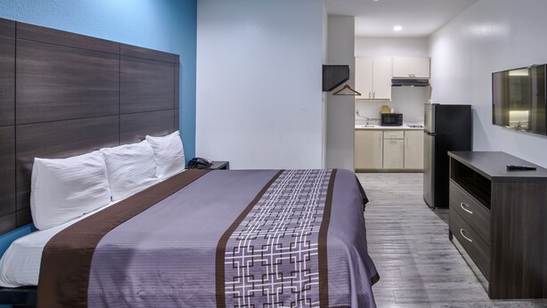 A hotel room with a bed, a desk, a TV, and a kitchenette in the background. - Lotus inn (Houston)