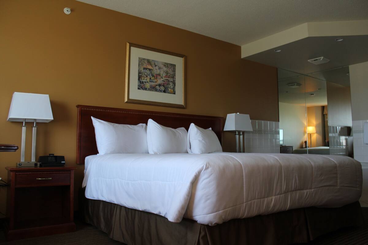 Un cuarto de hotel con una cama grande, dos mesas de noche, una mesita de noche, un cuadro en la pared y un espejo en la pared opuesta.