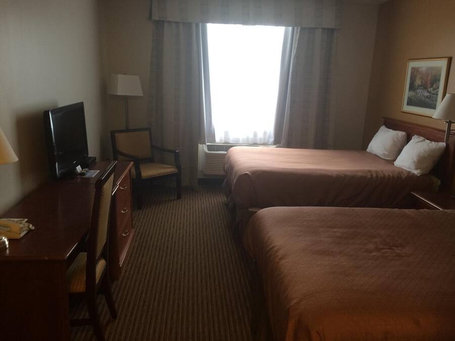 Habitación de hotel con dos camas, un escritorio, un televisor, una silla y un equipo de aire acondicionado.