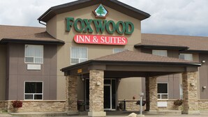 A Foxwood Inn & Suites building with a brown facade, stone pillars, and a covered entrance. - Foxwood Inn & Suites (Fox Creek)
