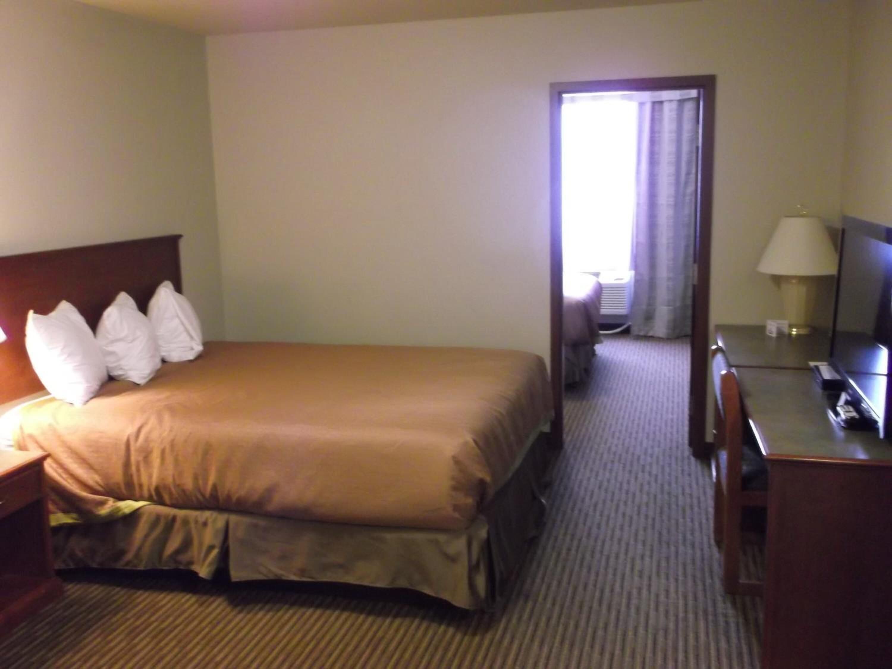 A hotel room with a bed, a desk, a chair, a TV, and a lamp.