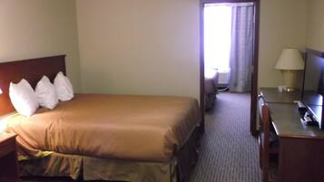 A hotel room with a bed, a desk, a chair, a TV, and a lamp.