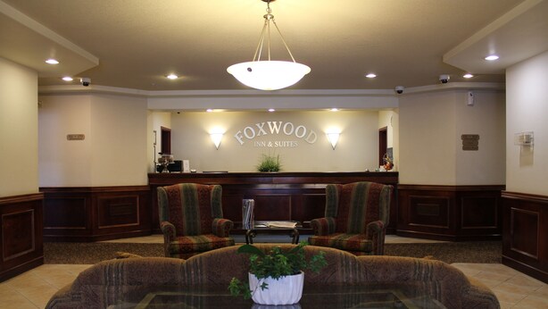 A lobby with a reception desk, two armchairs, a glass table with a plant, and a hanging light fixture. - Foxwood Inn & Suites (Fox Creek)