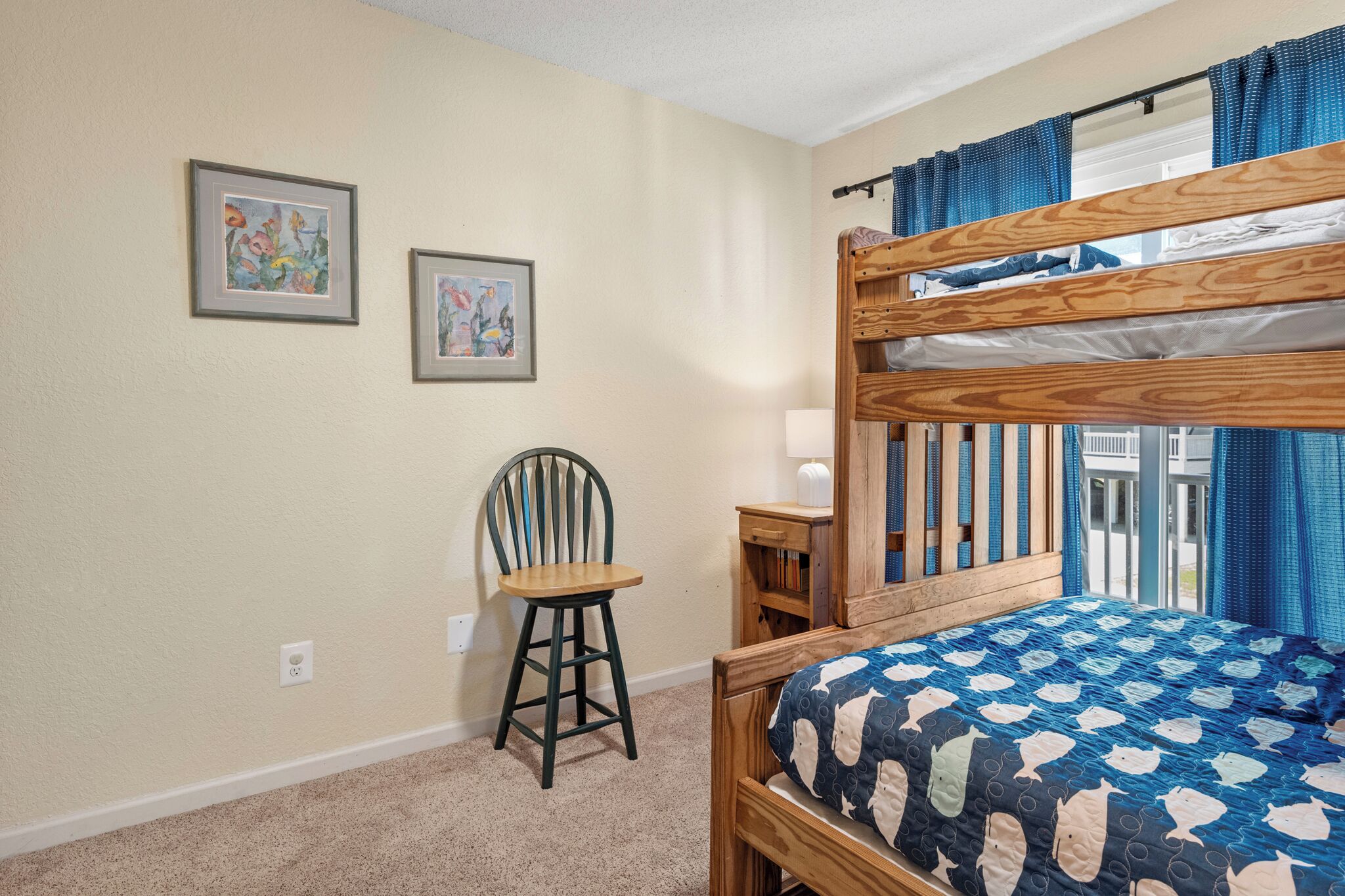 A bunk bed with a blue and white patterned bedspread, a wooden chair, and two framed artworks on the wall.
