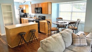A modern kitchen with wooden cabinets, a central island, and a dining area with a table and chairs. - Beautiful Branson Getaway! (Branson)