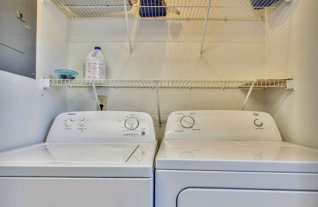 A laundry room with two front-loading washing machines and a metal shelf above them.