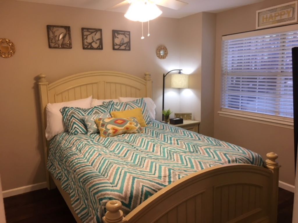 A bedroom with a bed, a nightstand, a lamp, and a window with blinds.