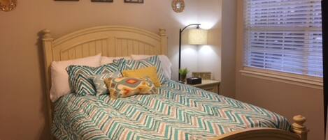 A bedroom with a bed, a nightstand, a lamp, and a window with blinds.