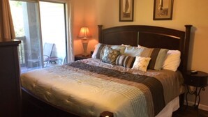 A bedroom with a large bed, a nightstand, a lamp, and a chair near a sliding glass door. - Beautiful Branson Getaway! (Branson)