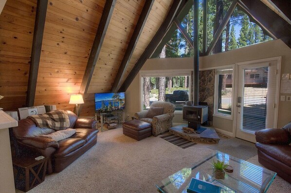Una sala de estar acogedora con techo alto, chimenea, televisor y vistas al exterior.