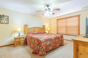 A bedroom with a bed, two bedside tables, a ceiling fan, a window with blinds, and a TV stand.