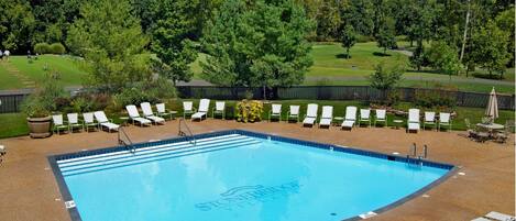 A rectangular swimming pool with a blue interior, surrounded by white lounge chairs and a paved deck.