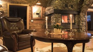 A cozy living room with a stone fireplace, leather armchair, and a round wooden table with candles. - - Take a break and reconnect at Farmhouse Kamovci21 - (Kamovci)