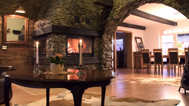 A stone fireplace with a fire, a dining table with chairs, and a cowhide rug. - - Take a break and reconnect at Farmhouse Kamovci21 - (Kamovci)