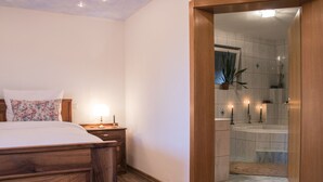 A bedroom with a wooden bed, a nightstand with a lamp, and a bathroom with a bathtub and a shower. - - Take a break and reconnect at Farmhouse Kamovci21 - (Kamovci)