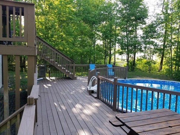 Une terrasse en bois avec une piscine, des bancs et un escalier menant à un espace abrité.