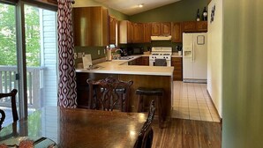 A kitchen with wooden cabinets, a central island, and a dining area with a table and chairs. - Heated pool-fire pit-central air-near PRNL (Christmas)