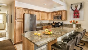 Una cocina moderna con armarios de madera, encimeras de granito y una isla central con taburetes de bar.