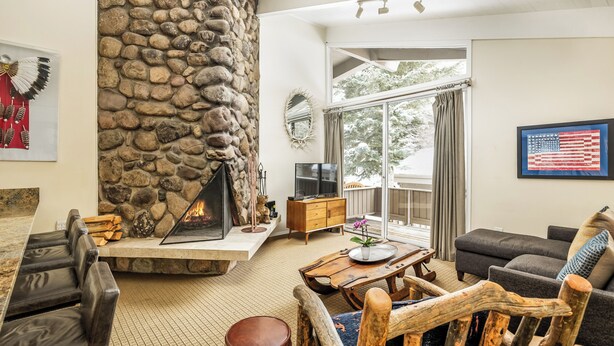 Una sala de estar con chimenea de piedra, televisor, ventana grande y una bandera en la pared.