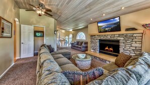 Una sala de estar amplia con chimenea de piedra, un televisor plano grande y un ventilador de techo.