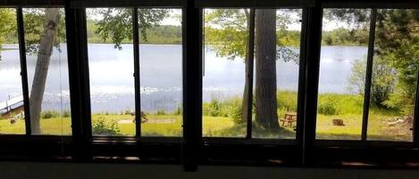 Une pièce dotée d’une grande fenêtre donnant sur un lac, avec un banc et une table de pique-nique à l’extérieur.