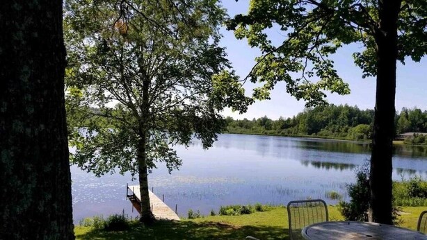 A lakeside setting with a table and chairs, a wooden deck, and a tree in the foreground. - Amazing sunsets/lake views - Near Pictured Rocks (Christmas)
