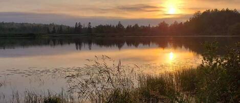 A calm lake at sunrise with a forested horizon.
