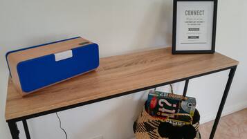 A wooden table with a blue speaker, a framed sign, and a woven basket with a DVD game box.