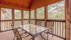 A covered patio with a glass-top table and metal chairs, surrounded by wooden railings and large windows.