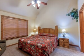 Une chambre à coucher avec un lit en bois, deux tables de chevet avec des lampes, un ventilateur de plafond, une fenêtre avec des stores et une porte.
