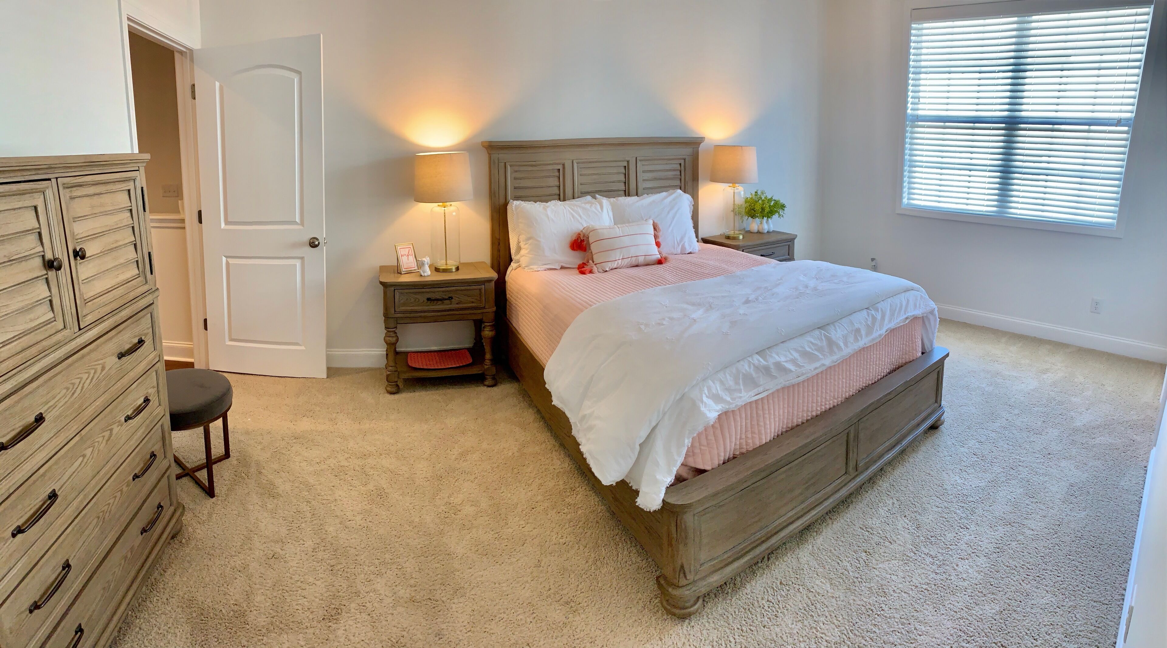 Une chambre à coucher avec un lit en bois, deux tables de chevet avec des lampes, une commode et une fenêtre avec des stores.